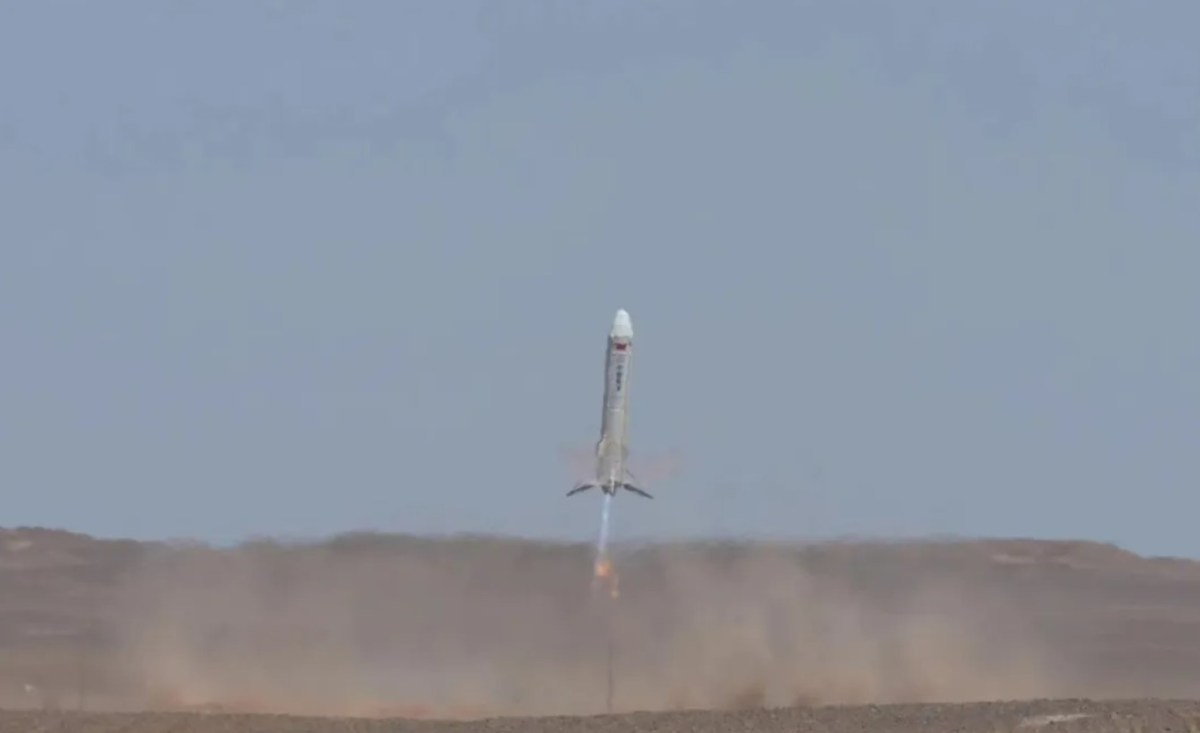 A SAST (Shanghai Academy of Spaceflight Technology) vertical takeoff, vertical landing (VTVL) rocket prototype during a test flight, kicking up dust from the ground. The rocket's engines emit a bright flame, indicating an active and controlled descent. The test was conducted in a desert-like environment under clear skies.