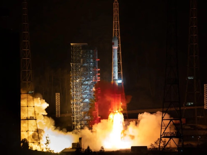 A Long March 3B rocket lifts off from the Xichang Satellite Launch Center at night, sending the Tianlian-2 (04) data relay satellite into orbit. Bright flames and smoke billow from the rocket’s base as it ascends past the illuminated launch tower.