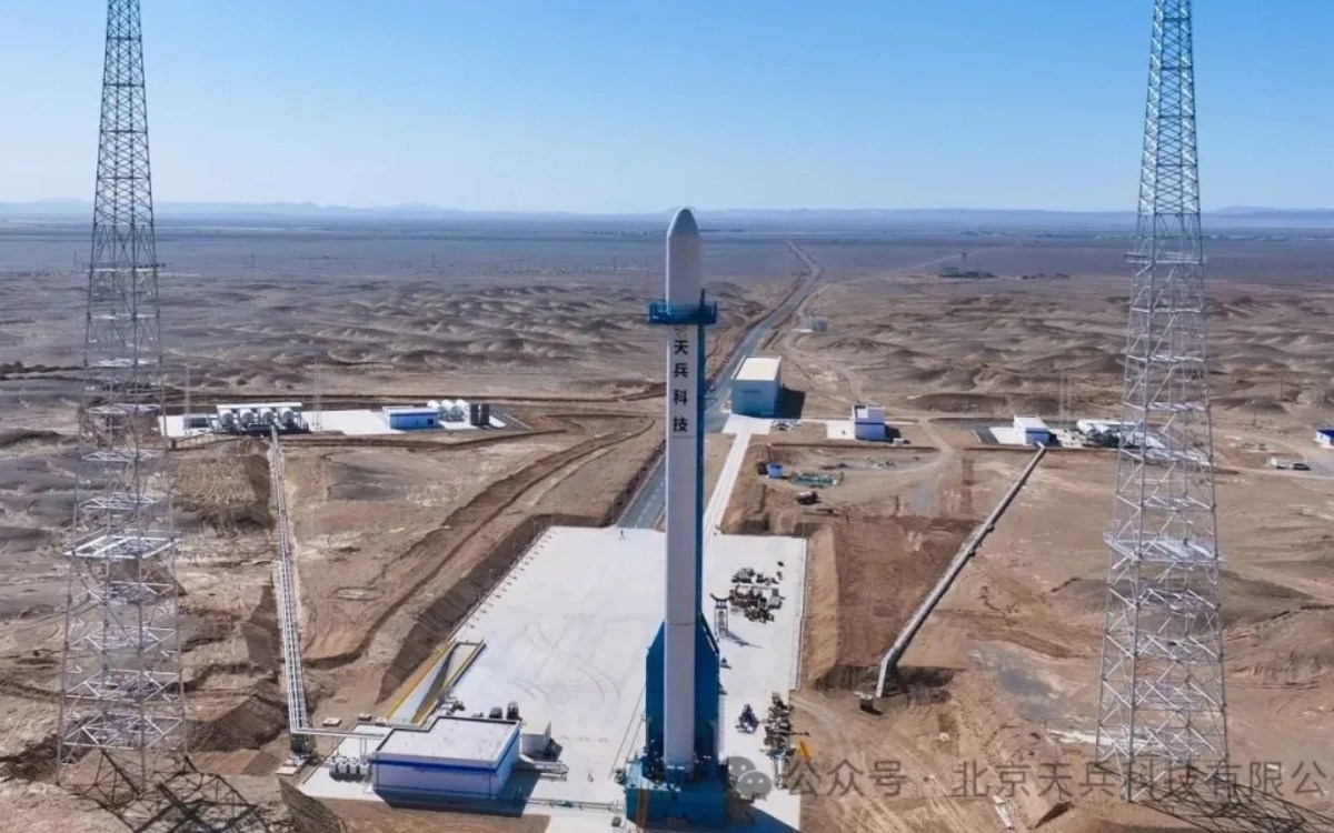Full-scale mockup of Space Pioneer's Tianlong-3 rocket stands vertically on a newly completed launch pad at the Dongfeng Commercial Space Innovation Test Zone, located in the desert landscape of Jiuquan Satellite Launch Center. The launch pad is equipped with support towers, fueling infrastructure, and ground facilities visible under clear blue skies.