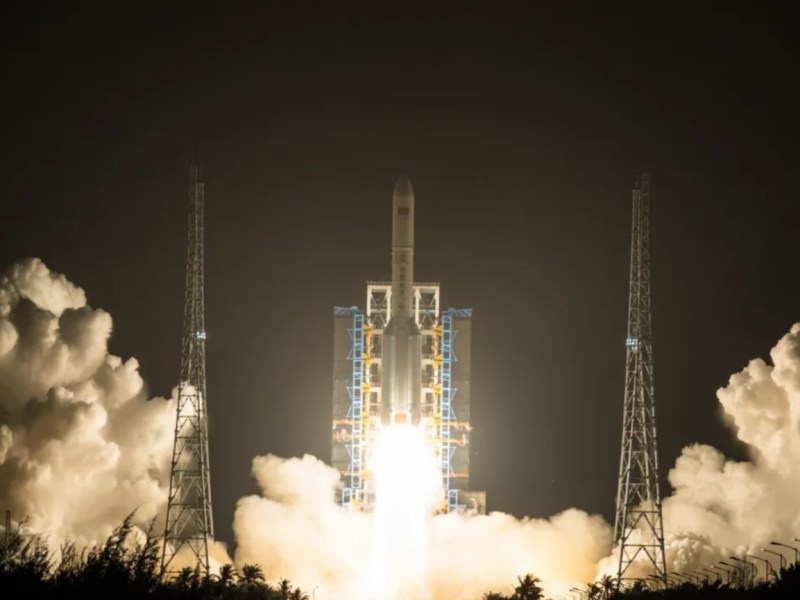 A Long March 5 rocket lifts off at night from the Wenchang Satellite Launch Center in Hainan, China, illuminating the launch pad with bright exhaust flames and surrounded by thick clouds of smoke.