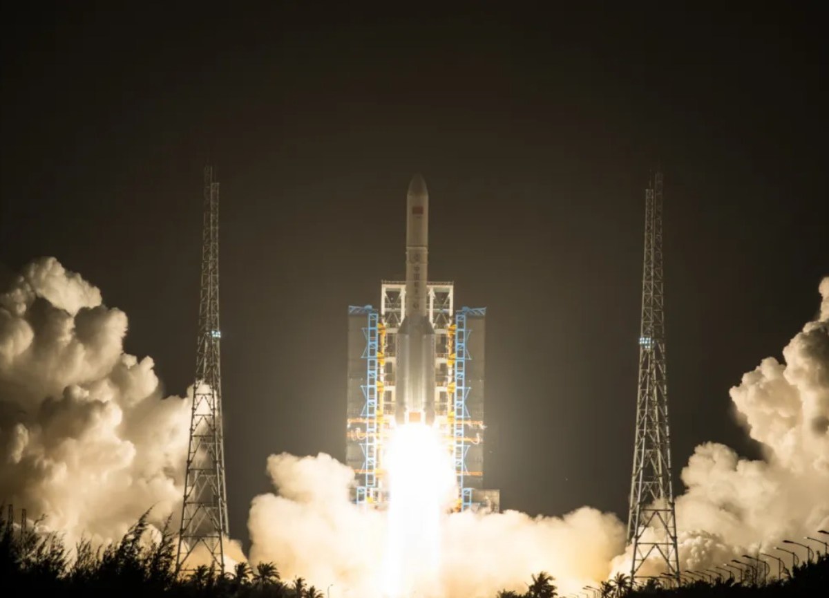 A Long March 5 rocket lifts off at night from the Wenchang Satellite Launch Center in Hainan, China, illuminating the launch pad with bright exhaust flames and surrounded by thick clouds of smoke.